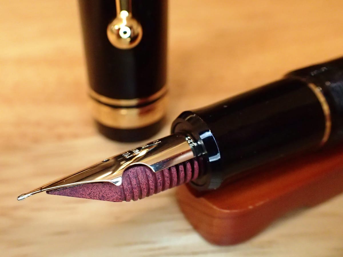 Macro shot of the nib and red ebonite feed of a Pilot Custom 742, with the cap sitting upright in the background