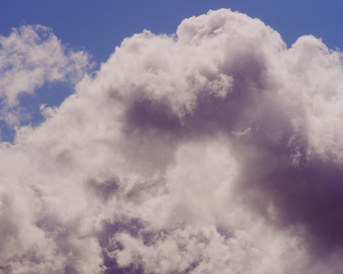 Telephoto view of poofy clouds in a blue sky, strongly lit by the sun