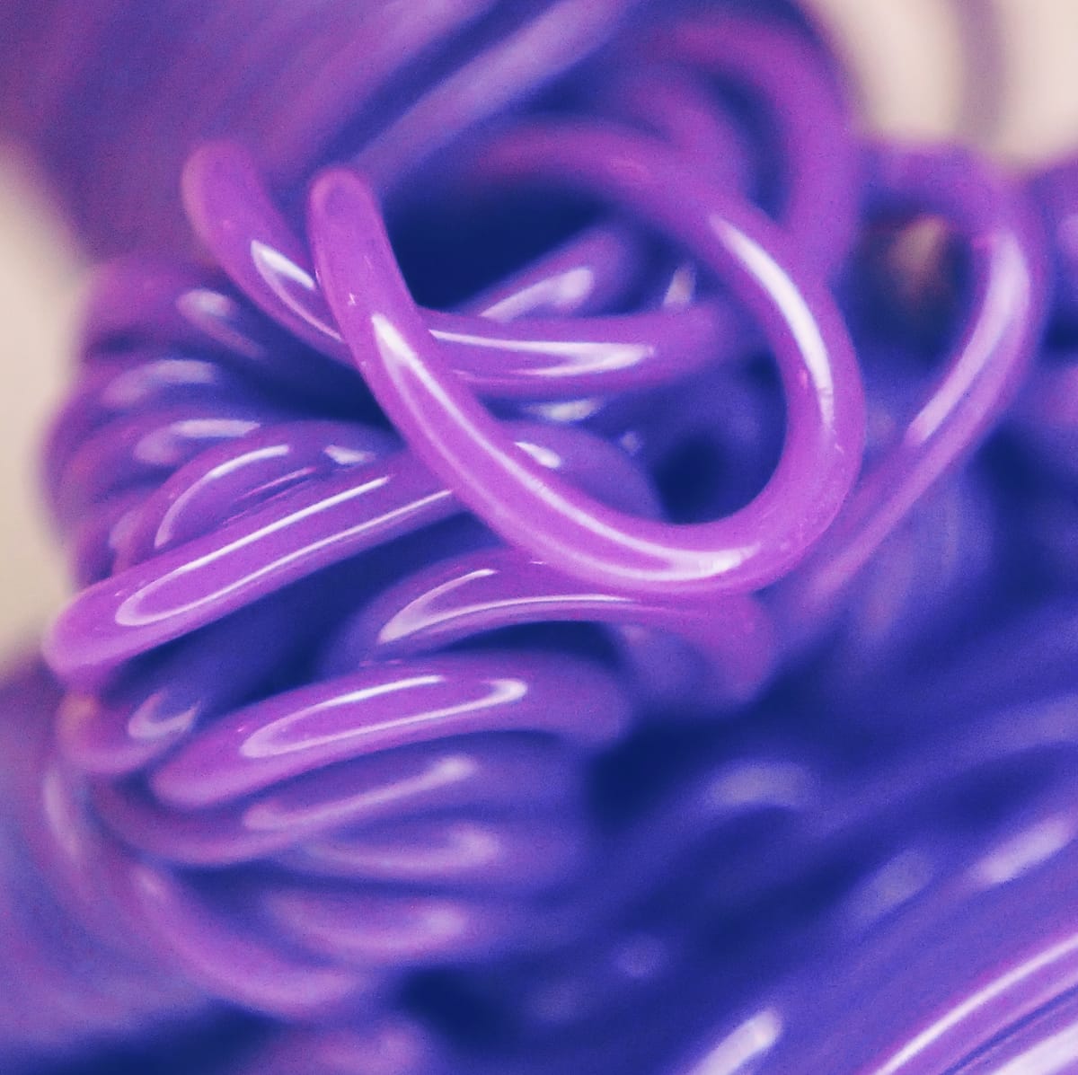 Macro shot of purple plastic melted into blobby loops by a 3D printer nozzle purge