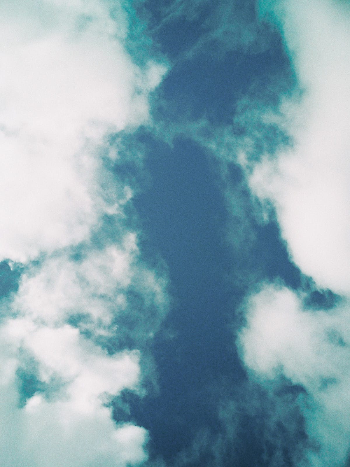 Looking up at white, puffy clouds framing a column of teal sky