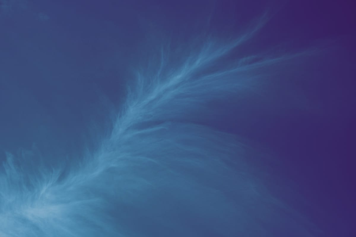 A very wispy cloud "spray" snaking diagonally across the frame from lower left to upper right; faint light blue against a dark blue-black sky