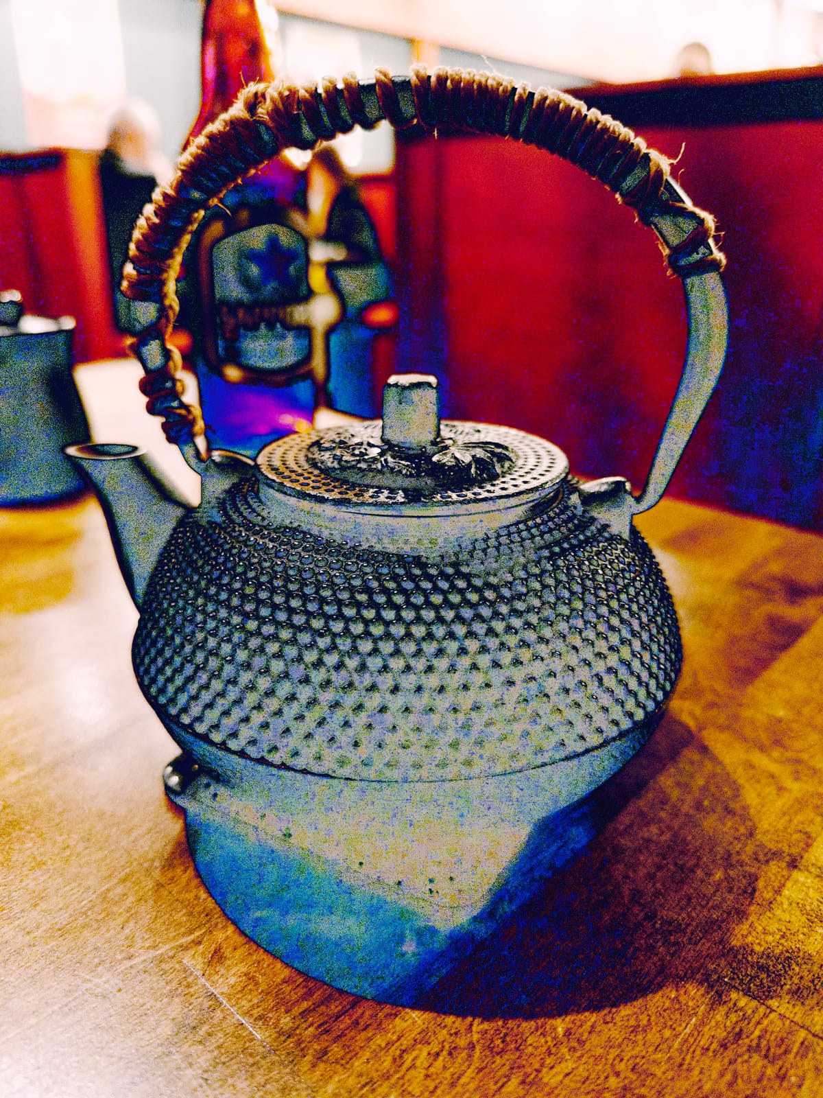 A Japanese cast iron (?) tea kettle sitting on a wooden restaurant table, the image colored surreally like an infrared heatmap