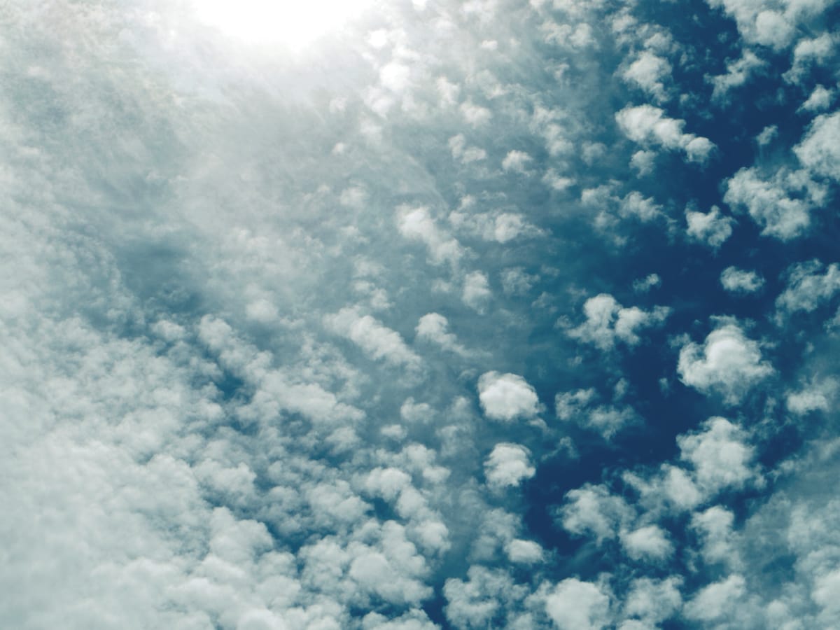Medium-blue afternoon sky filled with little white cotton-like clouds, the sun shining brightly at the top left edge of the frame