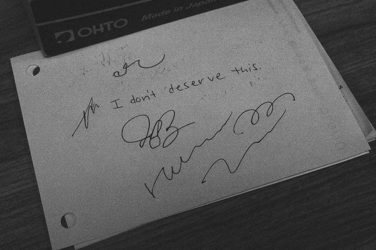 Black and white image of a scratch piece of paper at a pen testing station on which "I don't deserve this" along with random scribbles